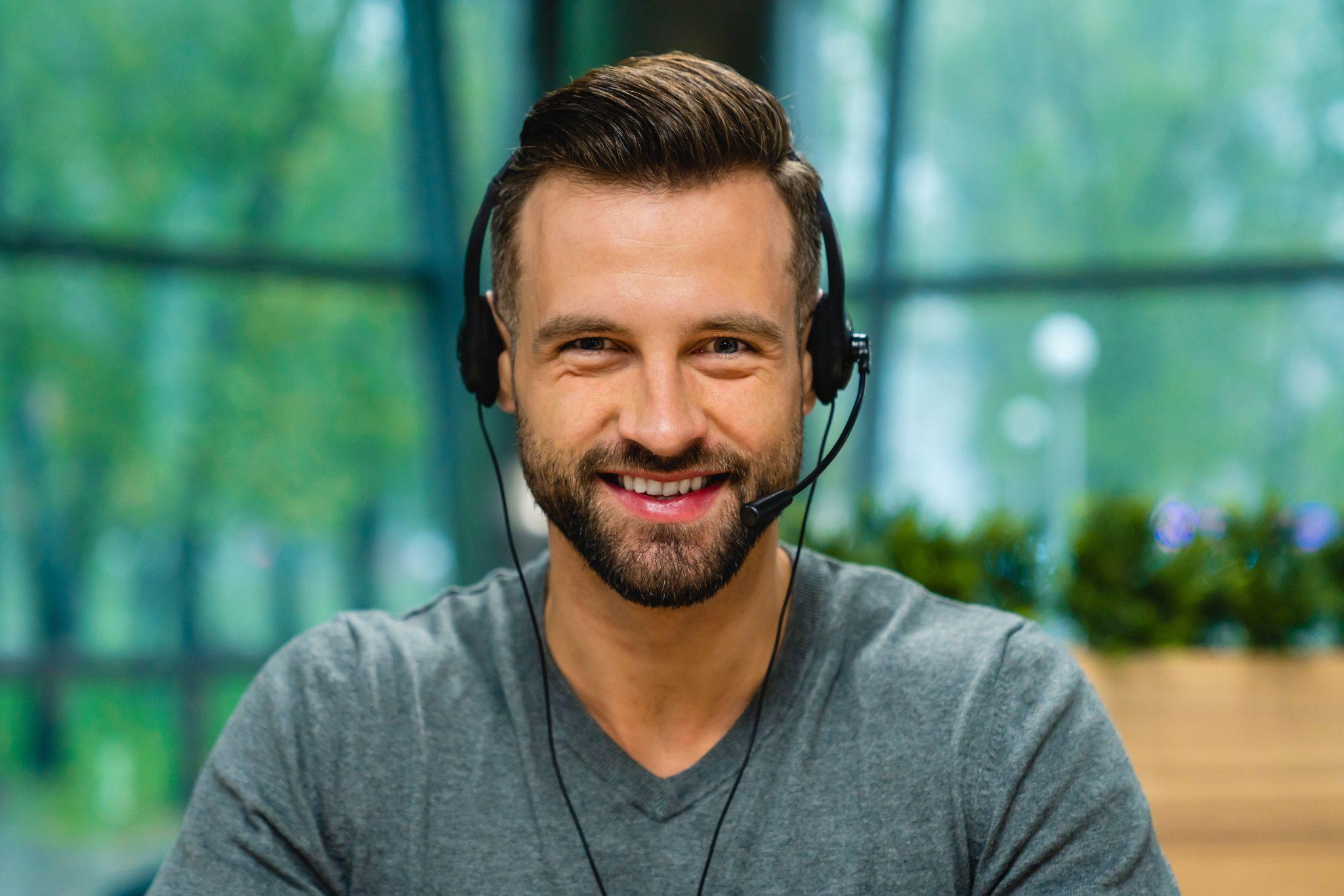 Close up portrait of young handsome man with beard and headset.