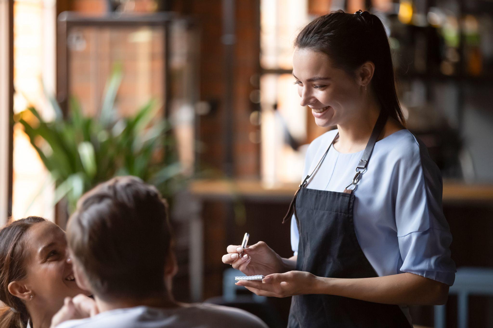 Smiling female waitress take order talk to clients.